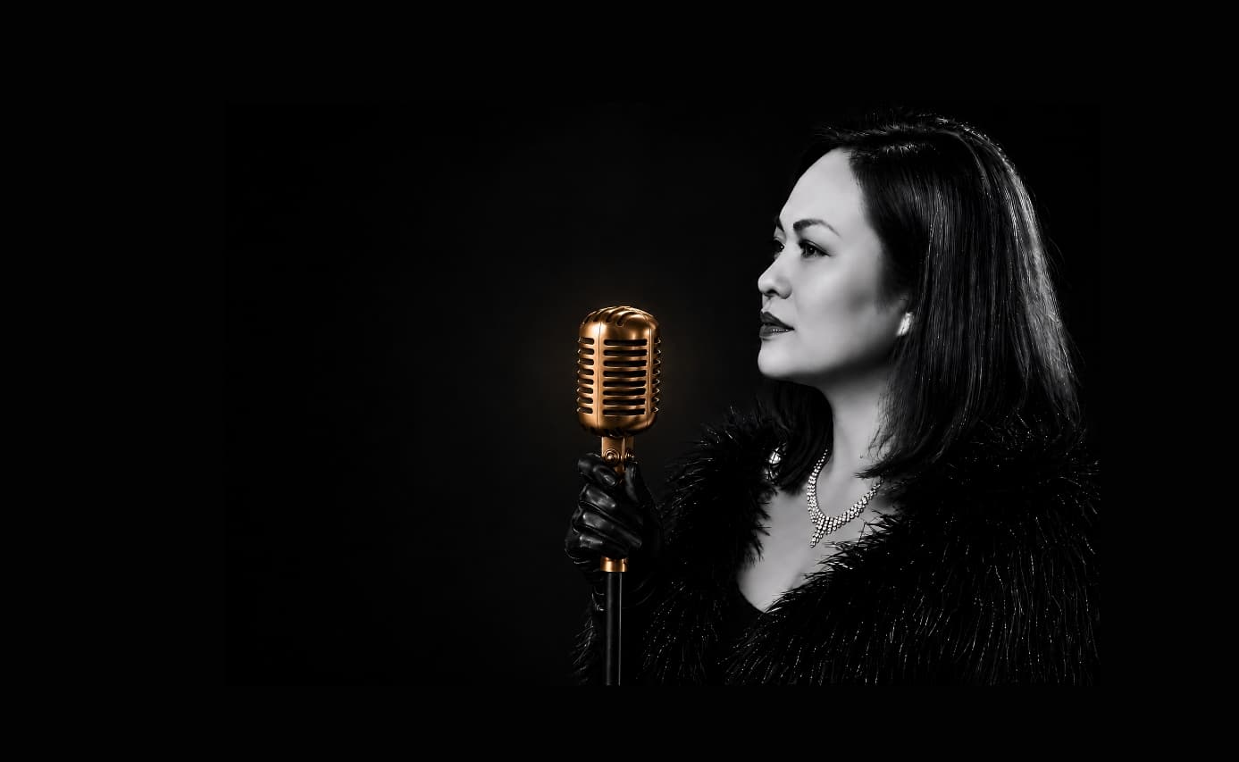 Vocalist in profile holding a vintage gold microphone, warm halo of stage light glowing from the mic.