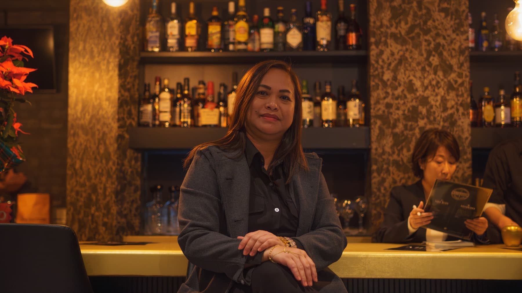 Guest at the bar counter with full whisky and wine shelves softly out of focus.