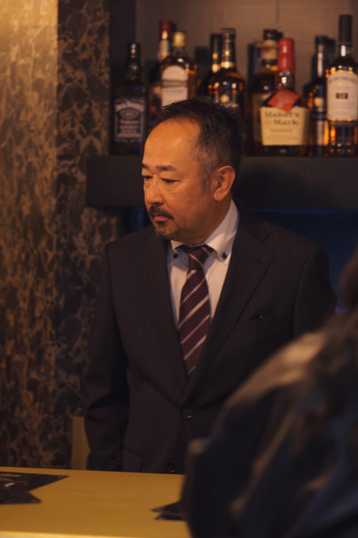 The whisky wall behind the bar — staff in front, deep shelves of bottles, warm pendant lights.