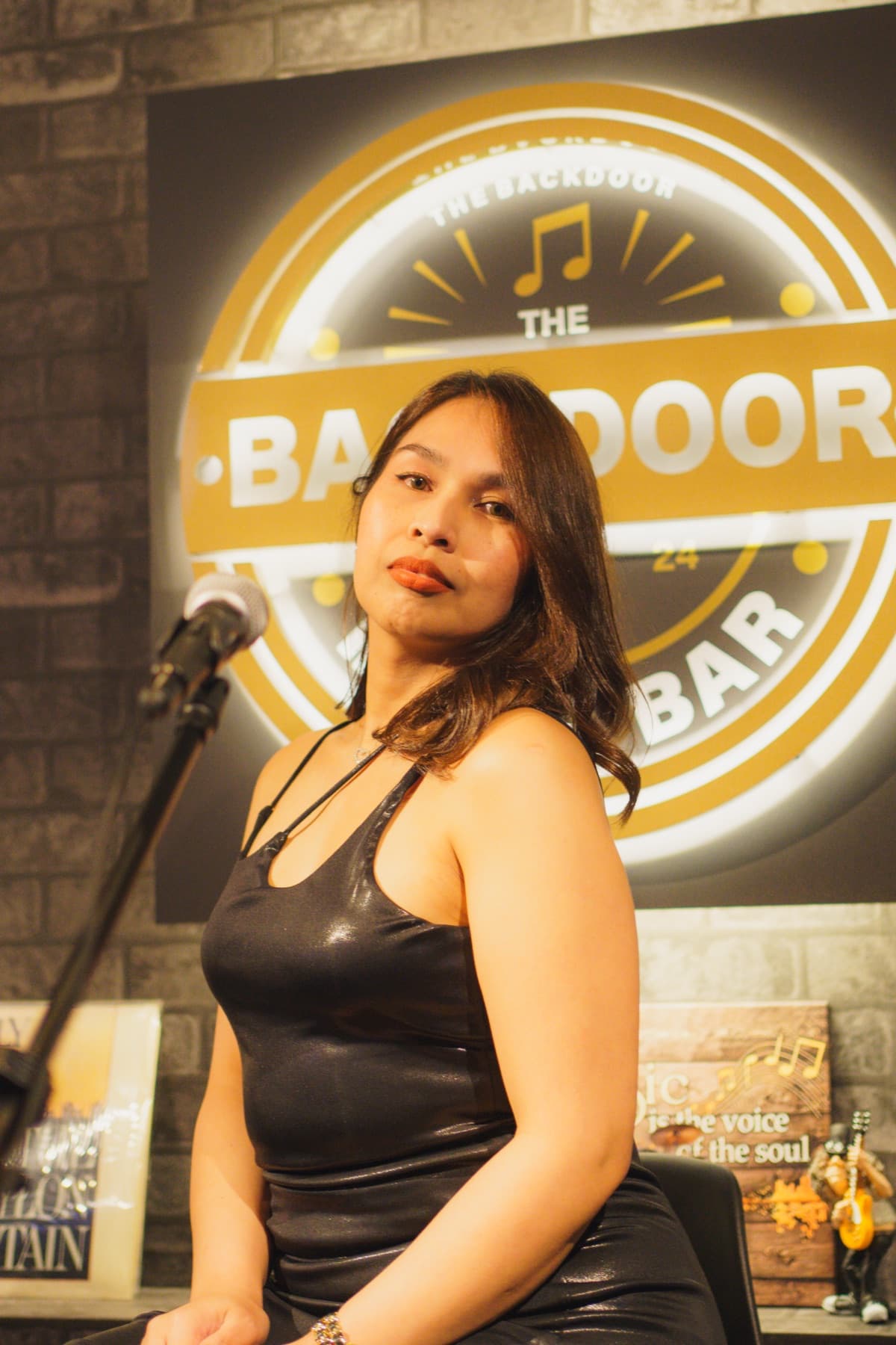 Vocalist in a black slip dress on the Backdoor stage, in front of the illuminated Backdoor logo, holding a microphone.