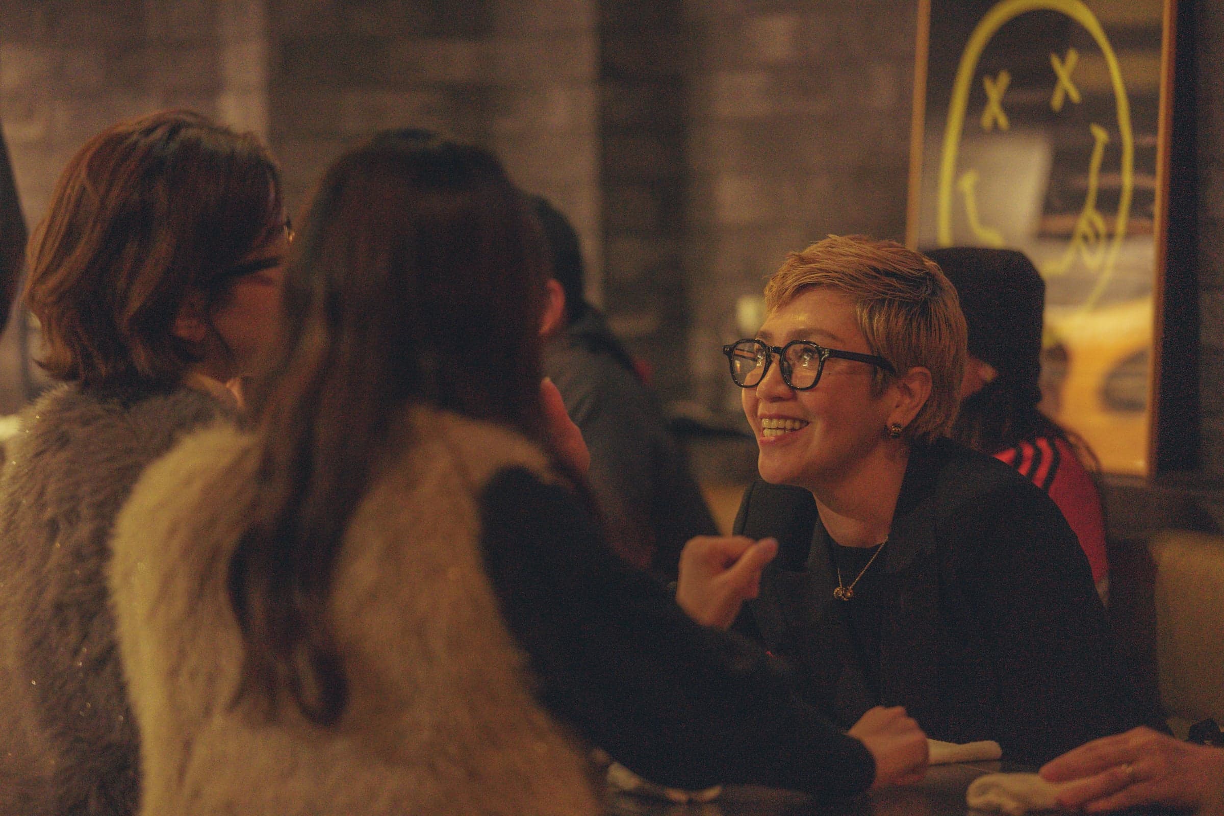 Three guests at a booth table at Backdoor, leather seating, the illuminated Backdoor sign behind them.